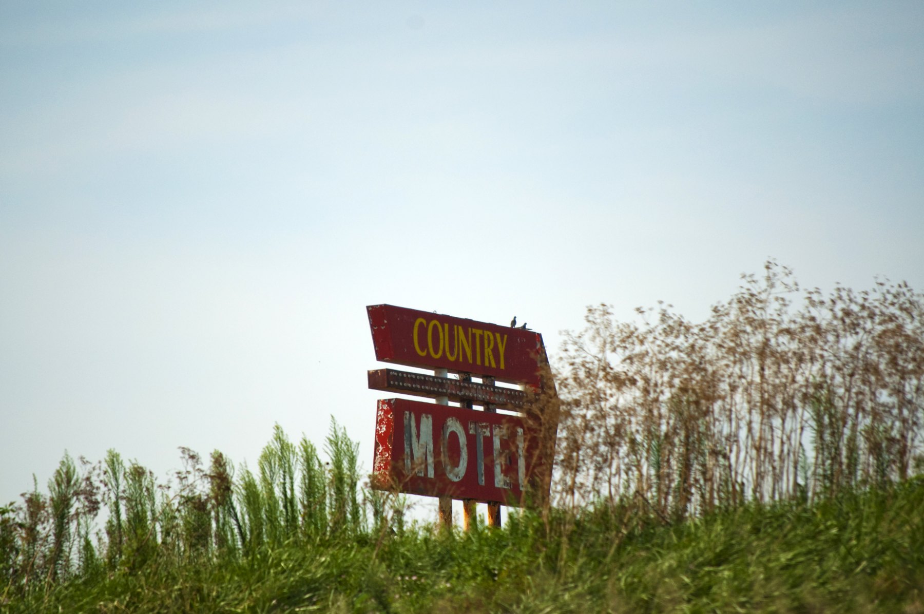 Weathered roadside motel sign in tall grass along the highway near Concordia, Missouri